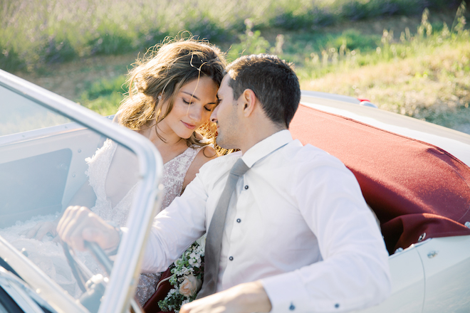 The bride and groom touching foreheads in the vintage car.