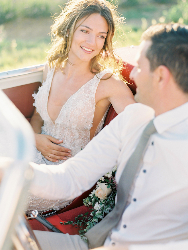 The bride smiling at the groom in a vintage car.