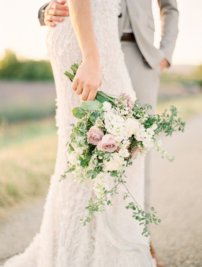 The groom holding the brides waist as she holds a bouquet for a romantic engagement editorial in the South of France.