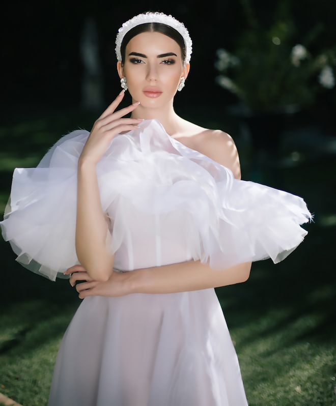 A woman wearing a wedding gown with tulle on the top and a white headband. 