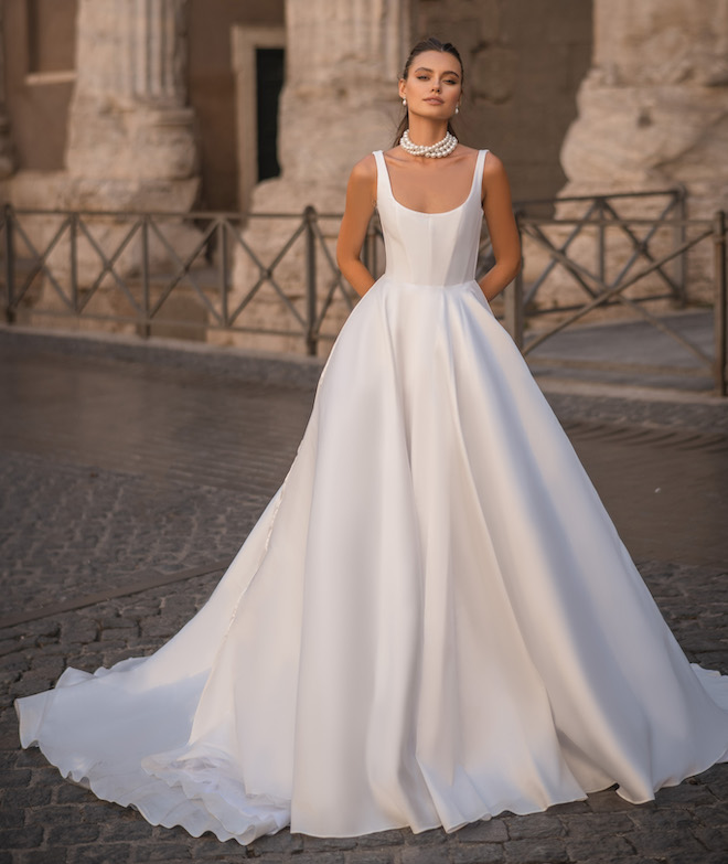 A woman wearing a satin wedding dress with a full skirt and a pearl necklace. 