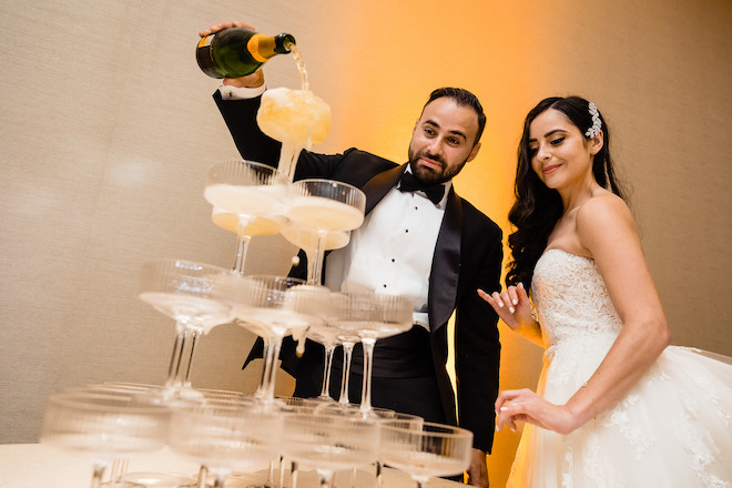 The bride and groom pouring champagne on a tower of glasses. 