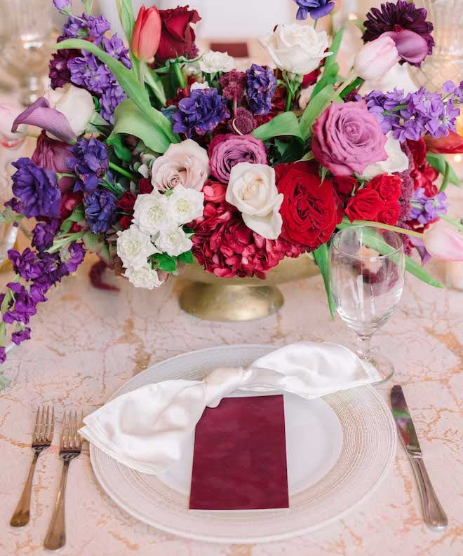 The table setting with white plates, maroon place setting and a floral arrangement at a luxurious Houston wedding.