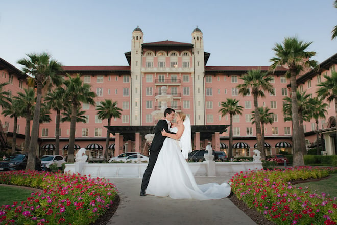 A groom dipping the bride in the center lawn at the Grand Galvez with a fountain and pink hotel in the background.