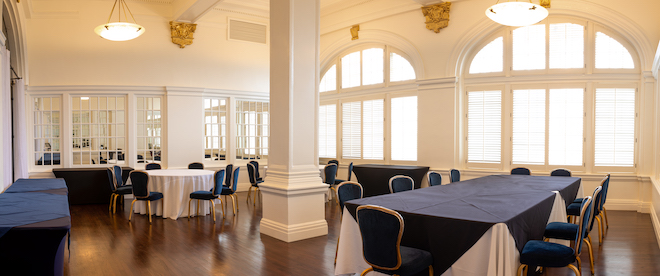 A ballroom with large windows and a mirrored wall with white and blue table linens. 