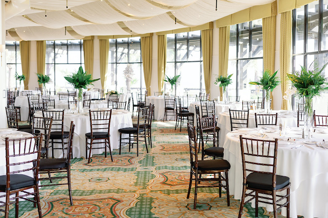 The Veranda in the Grand Galvez with floor to ceiling windows, yellow curtains, white round tables and greenery centerpieces.