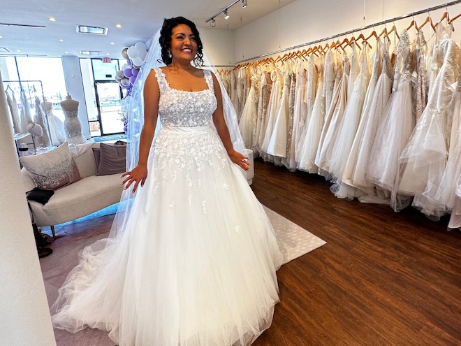 A bride smiling as she tries on a wedding dress in the bridal shop.