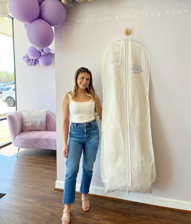 A bride smiling with her wedding dress zipped up in a bag from Luxe Redux Bridal.