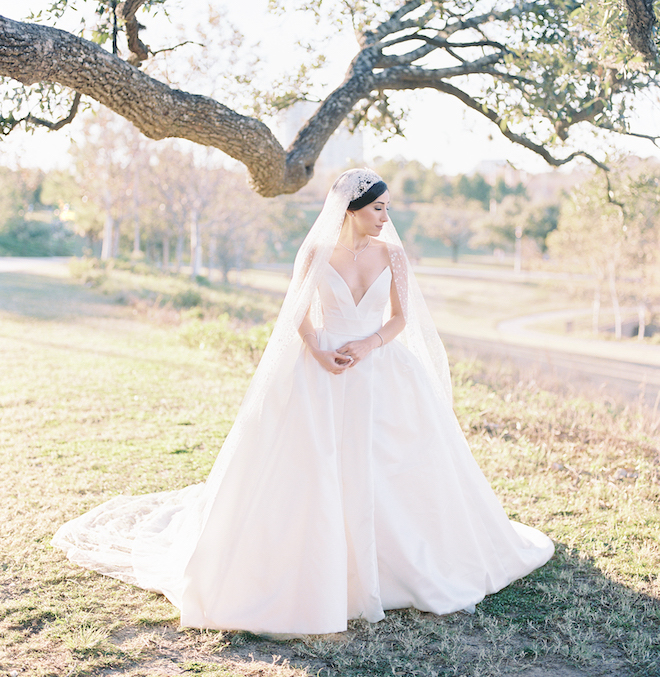 The bride standing in grass in front of a tree.