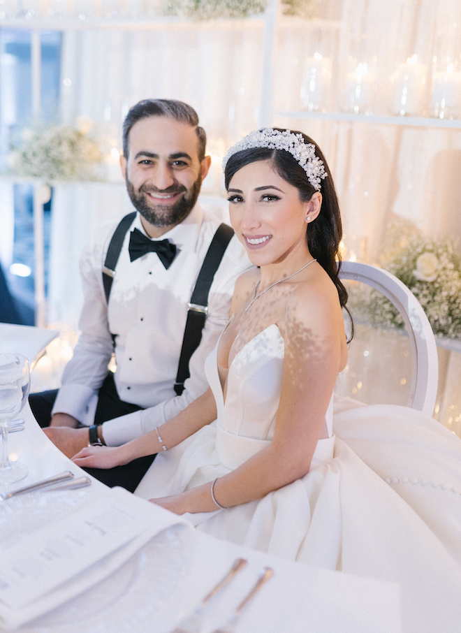 The bride and groom smiling sitting at the all-white wedding reception.