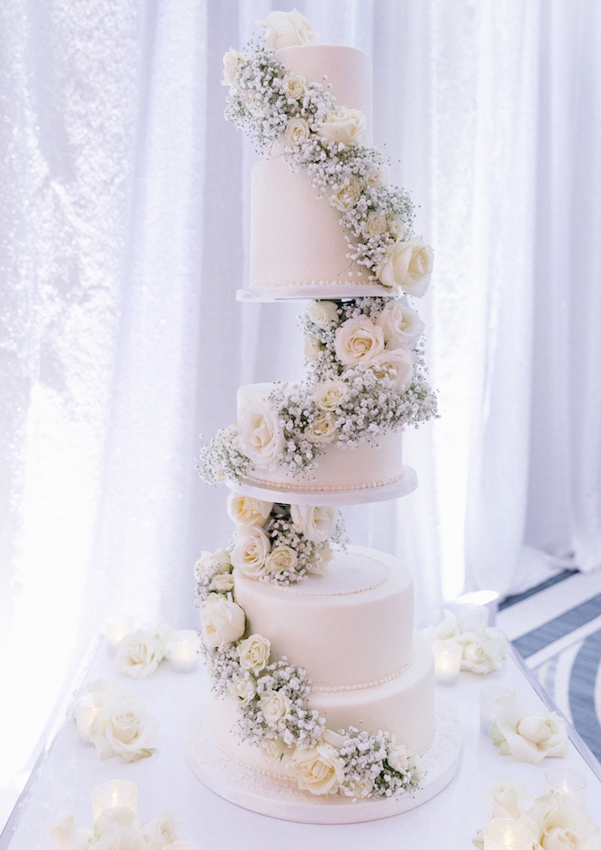 White five-tier wedding cake decorated with baby's breath and white roses at a wedding at Omni Houston Hotel. 