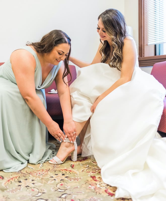 A bridesmaid helping the bride put on her shoe.