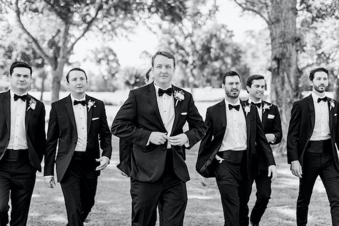 The groom walking with his groomsmen behind him.