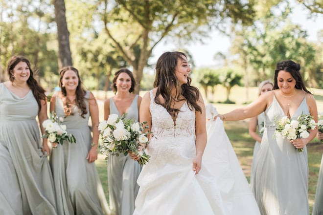 The bride and her bridesmaids in sage dresses walking outside before the white sage and blush wedding.