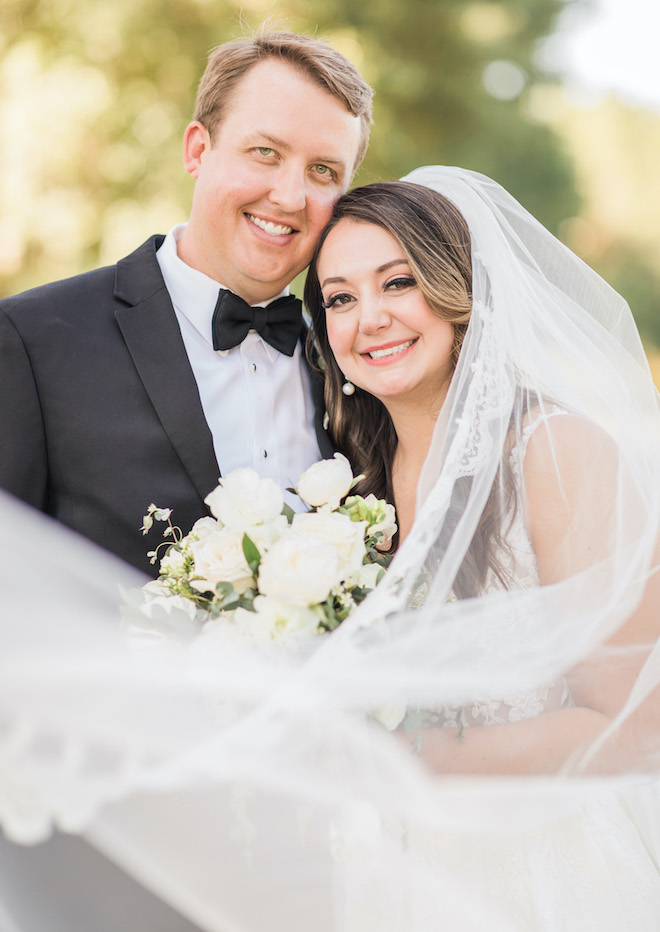 The bride and groom smiling with the brides veil flowing on front of them.