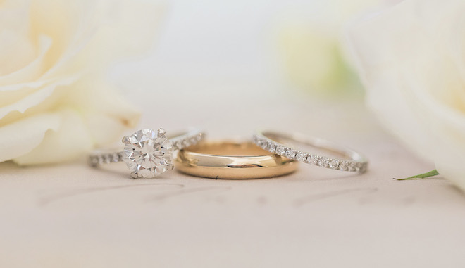 The brides engagement ring and wedding band resting on the groom's gold band.