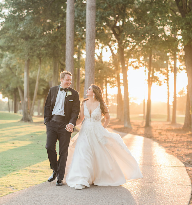 The bride and groom holding hands walking outside during sunset. 
