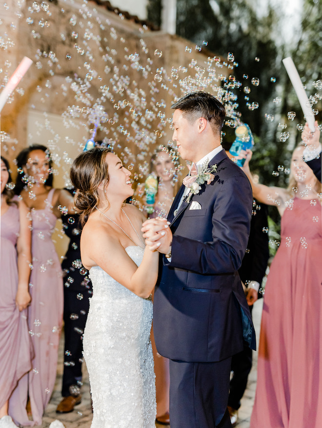 The bride and groom holding hands and smiling at each other during a bubble send off. 