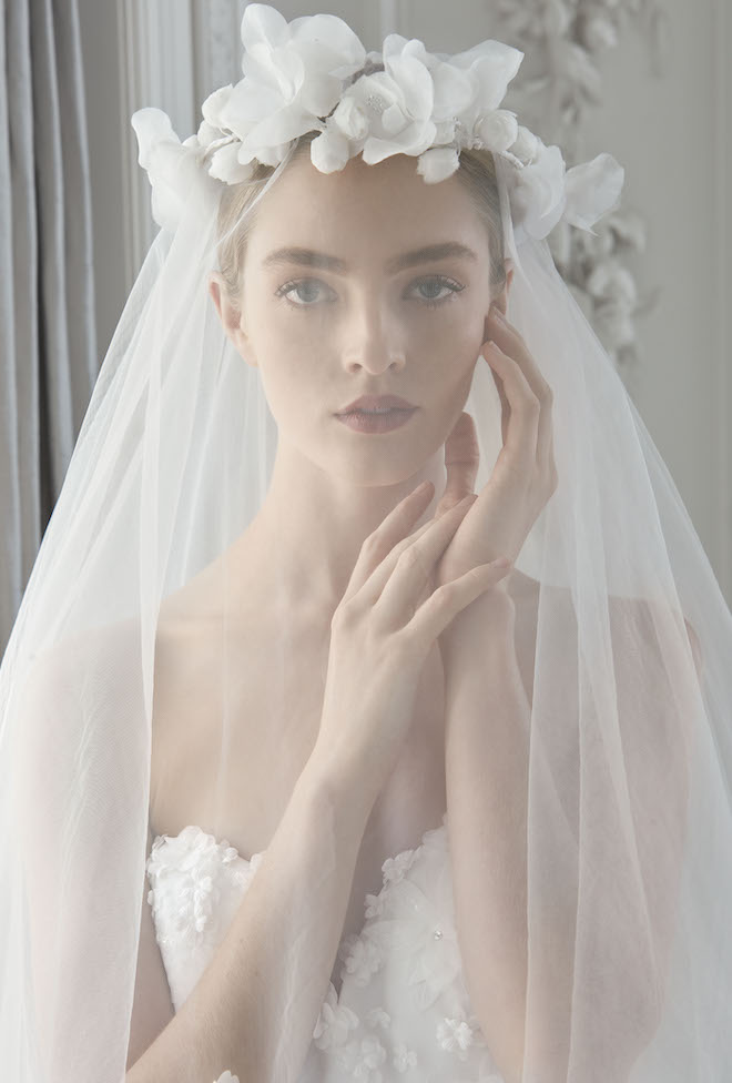A woman touching her cheek with a white flower crown veil over her face. 
