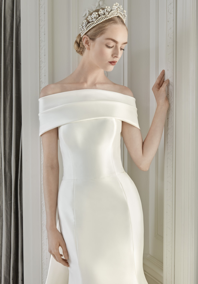 A woman looking down wearing a satin strapless wedding dress with a pearl tiara.