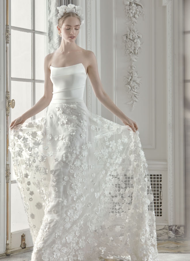 A woman wearing a Sareh Nouri wedding gown with a structured top and a floral applique skirt. 
