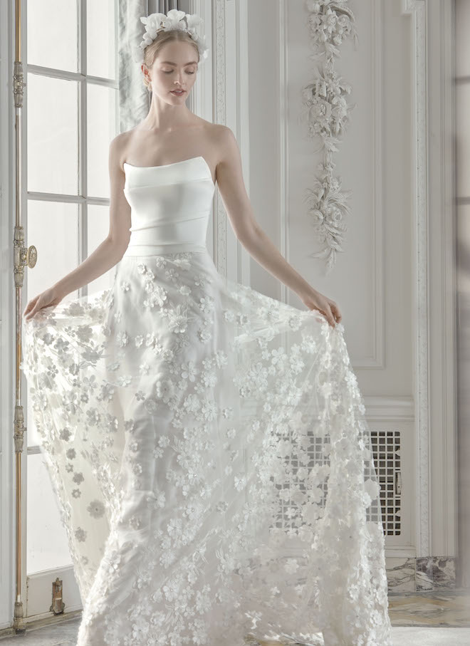 A woman wearing a Sareh Nouri wedding gown with a structured top and a floral applique skirt.