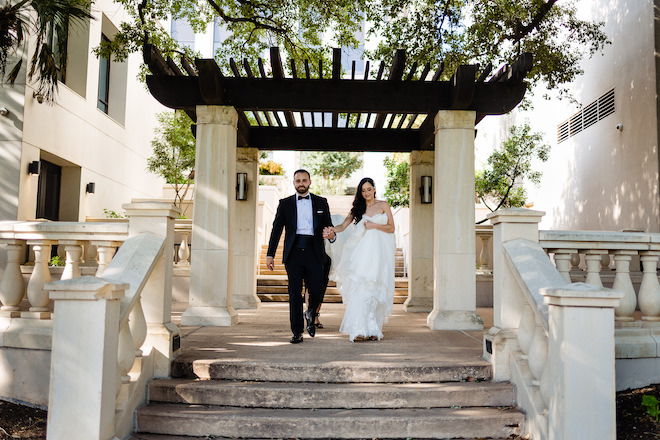 The bride and groom holding hands about to walk down stairs outside. 