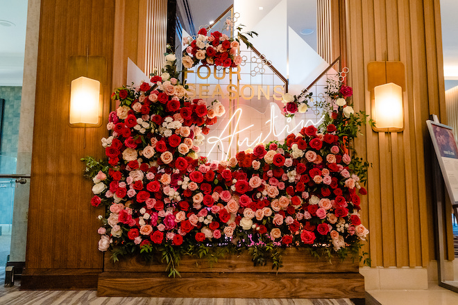 A flower wall with red and pink roses and a sign saying "Four Seasons Austin"