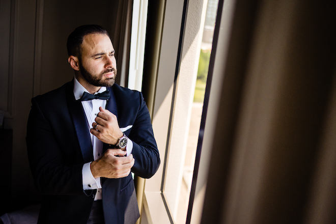 The groom adjusting his watch and looking out the window. 