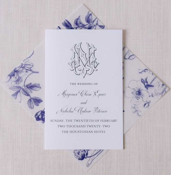 A white invitation with black cursive for Nick and Margeaux's wedding with their monogram on top of the invitation. The envelope is a blue and white floral print. 