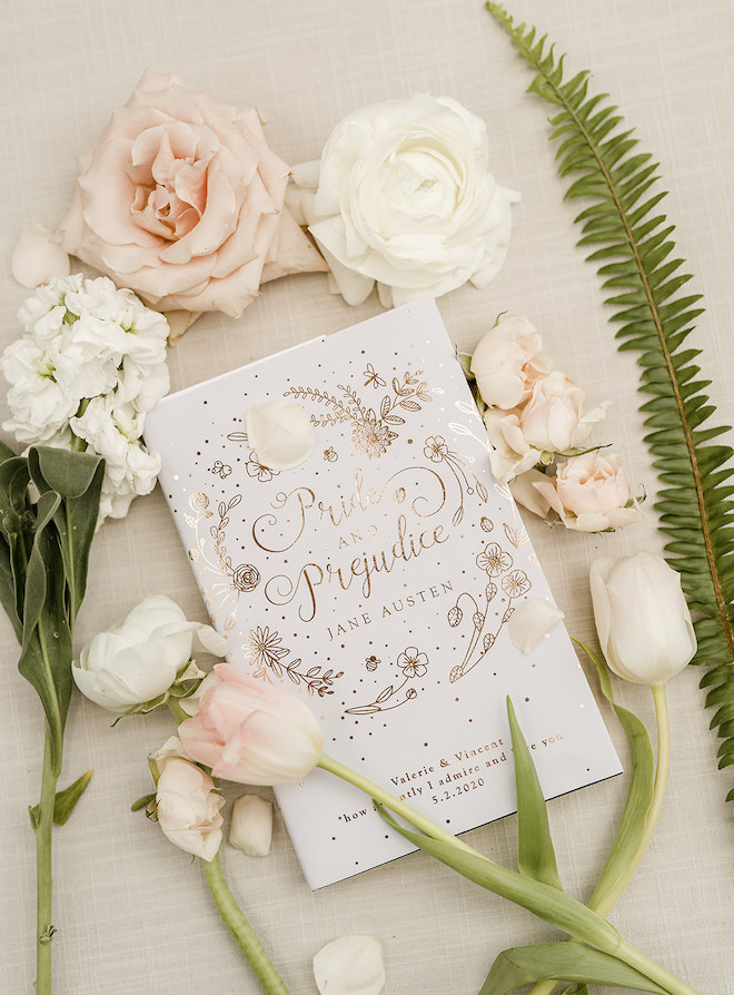 A white wedding program with a gold design that resembles "Pride and Prejudice" by Jane Austen. 