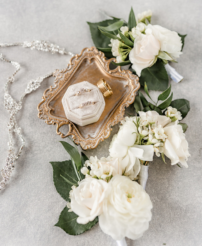 A flat lay including white florals and the wedding rings on a gold tray.