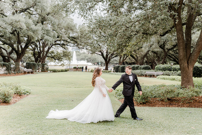 The bride and groom walking in a field with a fountain in the background before their wedding at Rice University. 