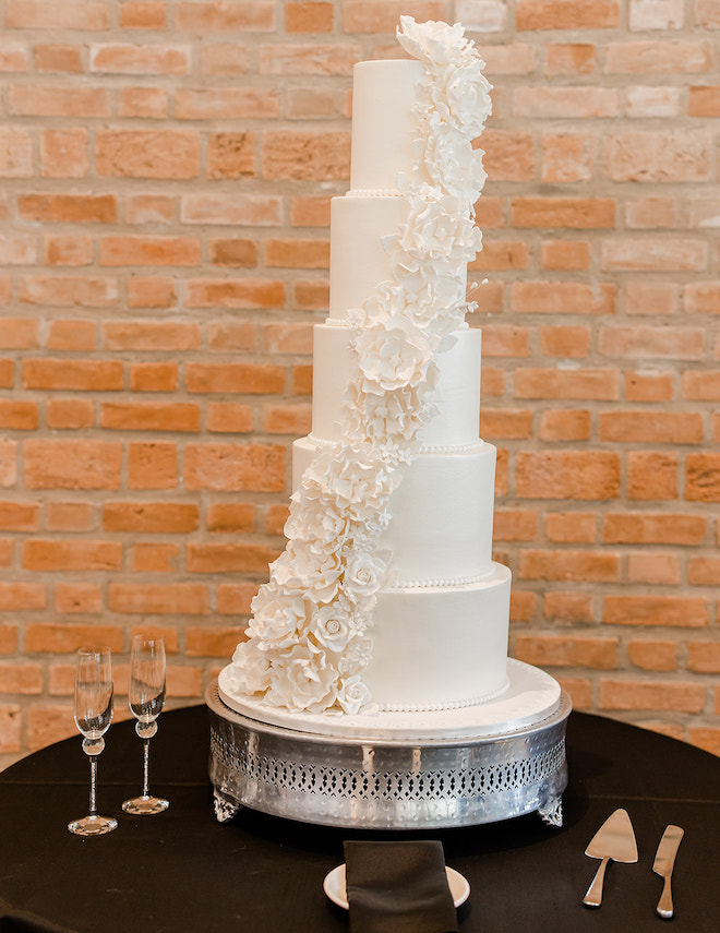 A five tier white wedding cake with white florals garnishing each tier. 