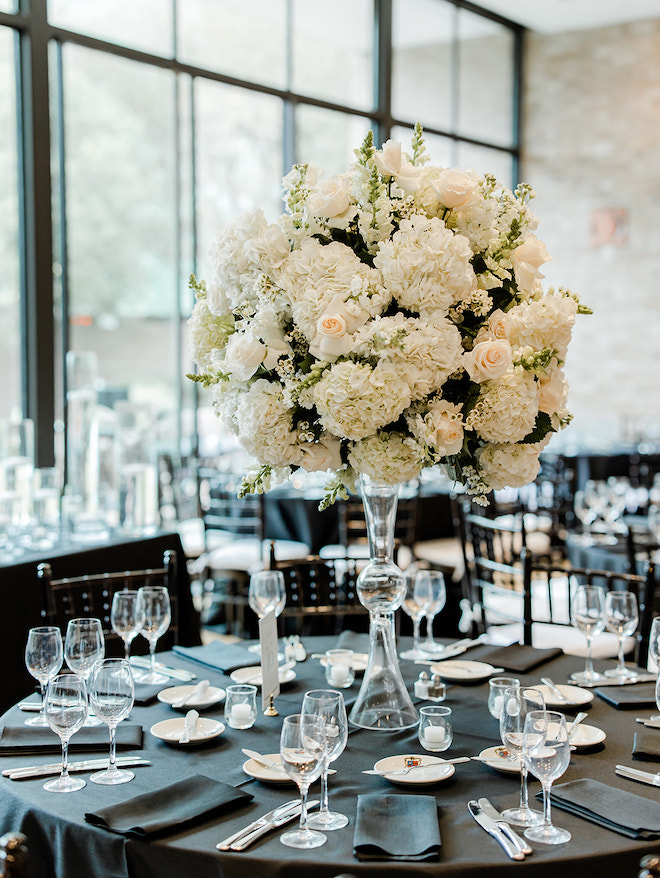 A circular reception table with black linens and a large white hydrangea centerpiece. 