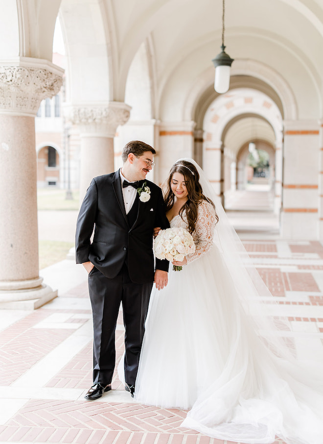 The bride and groom walking under the arches of Rice University. 