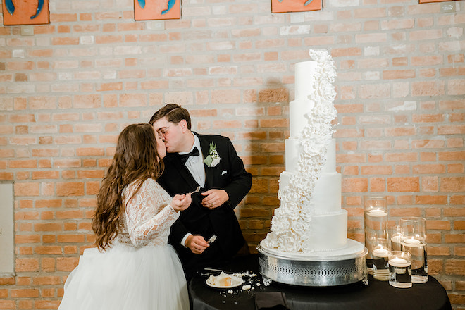 The bride and groom kissing in front of a five tier white wedding cake. 