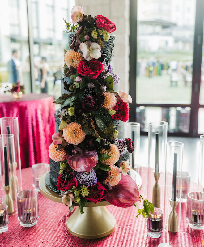 A four tier black cake with magenta and peach florals with greenery. 