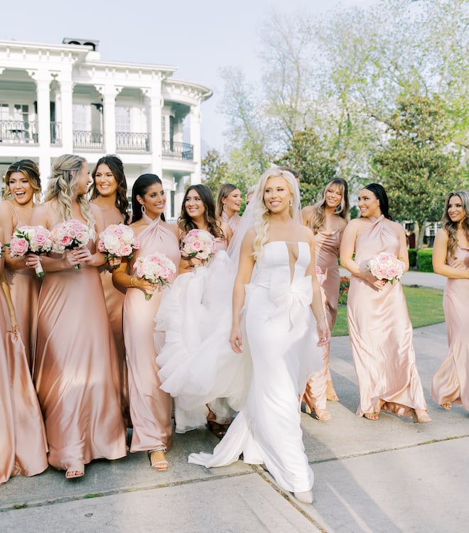 The bride walking in front of her bridesmaids in pink satin dresses.