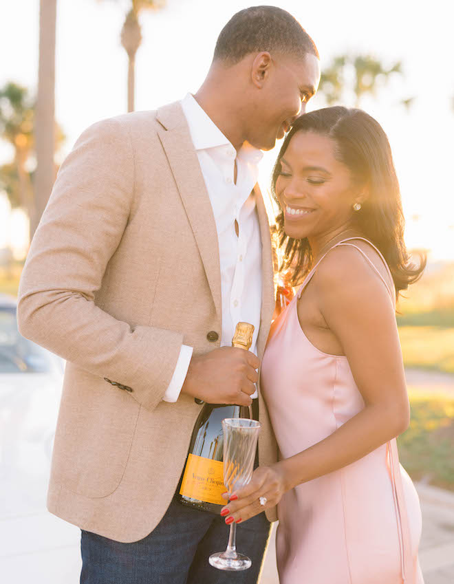 A couple smiling as the man holds a champagne bottle and the woman holds a champagne glass.