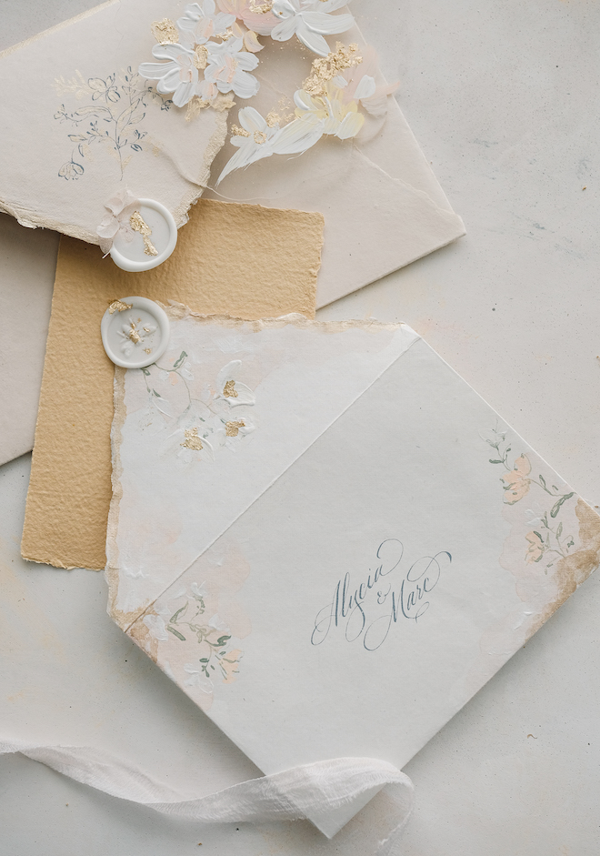 Two envelopes with a name written in cursive and white, blush and gold flowers decorating the envelope. 