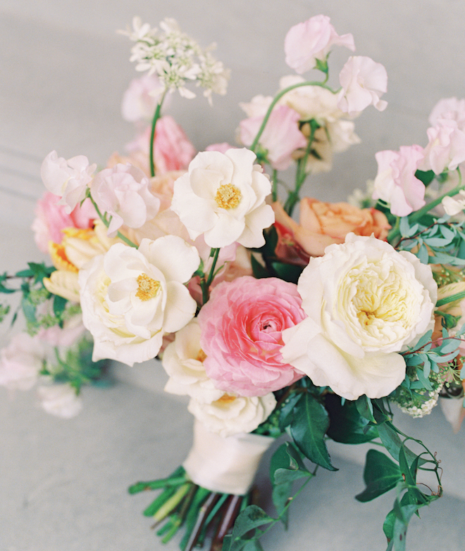 A bouquet with white, orange and pink florals and trailing greenery. 