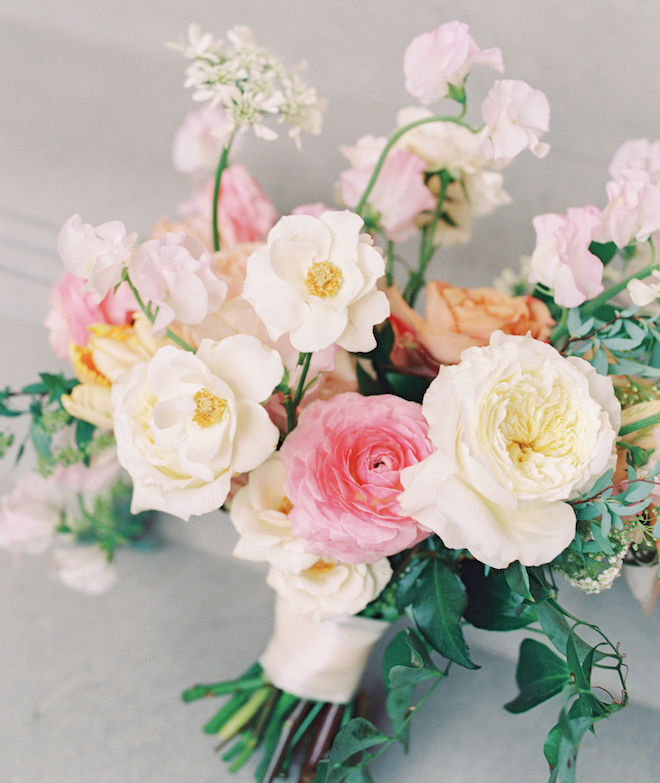 A bouquet with white, orange and pink florals and trailing greenery.