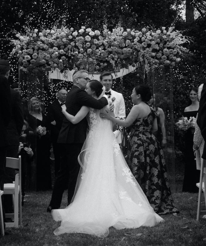 The bride and her father hugging in front of the floral-filled chuppah. 