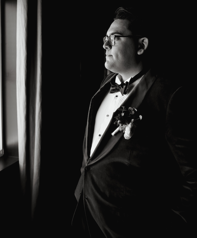 A black and white photo of the groom looking out a window.