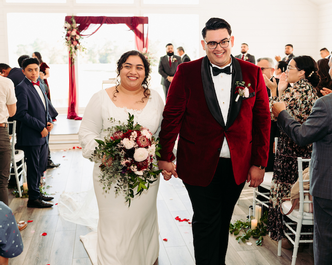 The bride and groom holding hands as they walk down the aisle and guests clapping. 