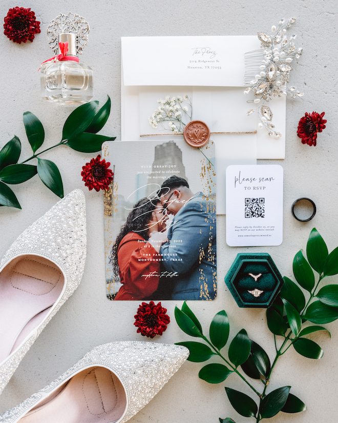 An invitation suite with a photo of the couple, a QR code and a emerald green ring box. Sparkly heels, a perfume bottle and a hair accessory are surrounding the invitation.