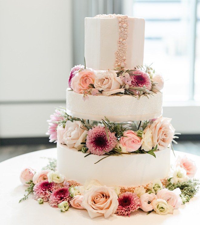 Three tier white wedding cake decorated with pink pearlized candies and fresh pink and magenta florals by For Heaven's Cake at a wedding styled shoot at The Laura Hotel in Houston.