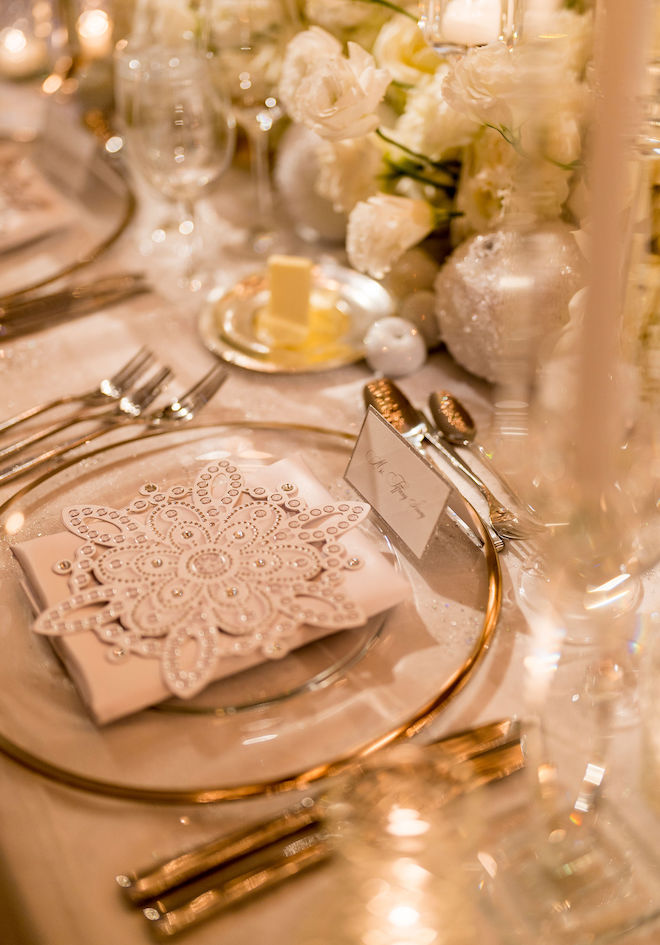 A clear plate with a gold rim with a napkin and a snowflake cutout on top of it. 