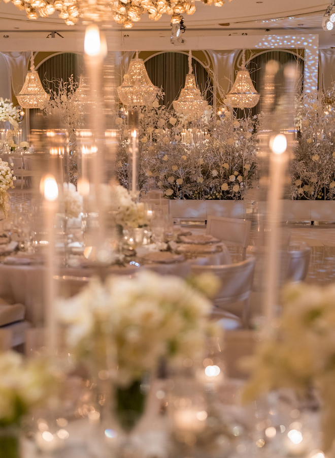 White florals, pillar candles and grand chandeliers decorating the reception space.